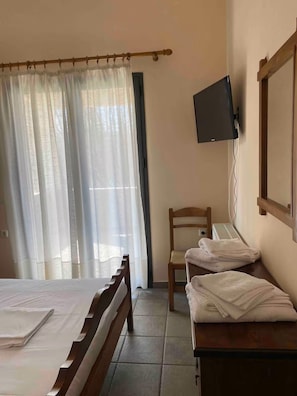 Hotellihuone, jossa on sänky, tuoli, seinälle asennettu televisio ja ikkuna, jossa on verhot.