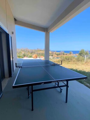 Une table de ping-pong sur un balcon offrant une vue dégagée sur la mer et le paysage environnant.
