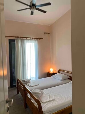 Une chambre avec deux lits, un ventilateur de plafond, une fenêtre avec des rideaux et une lampe de chevet.