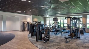 Ein Fitnessstudio mit verschiedenen Trainingsgeräten, einem gewölbten Holzboden und großen Fenstern, die für natürliches Licht sorgen.