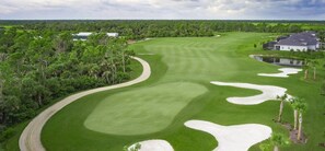 Ein Golfplatz mit gewundener Bahn, Sandbunkern und einem großen Haus im Hintergrund.