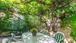 Um pátio externo com mesa redonda e cadeiras, rodeado por vegetação e uma parede de pedra.