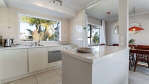 Een moderne keuken met witte kasten, een groot raam en een eethoek met houten stoelen.