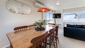 Een eetgedeelte met een houten tafel, stoelen, een vaas met bloemen, een spiegel en een televisie.