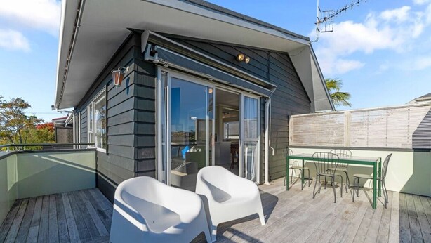 Een modern huis met een terras, twee witte stoelen en een tafel.