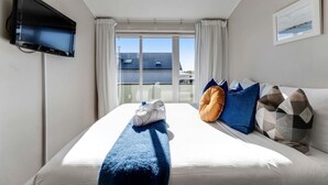 Een hotelkamer met een bed, een aan de muur bevestigde televisie, een raam met gordijnen en een balkon met uitzicht.