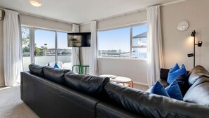Een moderne woonkamer met een leren bank, een flatscreen televisie en een stadszicht door grote ramen.