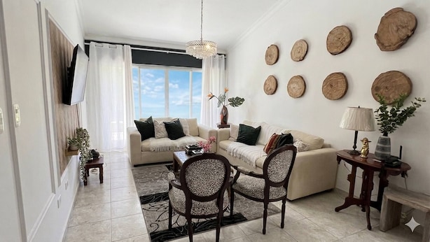 A living room with a sofa, chairs, a coffee table, a TV, and decorative wall art. - The Distrito Atelier (Santo Domingo)