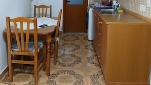 A compact kitchen with a dining table, chairs, a washing machine, and patterned floor tiles. - Enjoyable 1-bedroom apartment with AC in charming Berat (Berat)