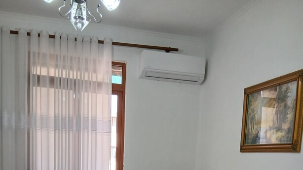 A hotel room with a bed, a wooden headboard, a painting on the wall, and an air conditioning unit. - Enjoyable 1-bedroom apartment with AC in charming Berat (Berat)