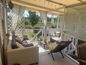 Ein überdachter Außenbereich mit einer Couch, einem Sessel und einem Tisch mit Blick auf einen Garten.