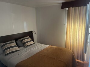 Ein Hotelzimmer mit Bett, Kopfteil, einem Fenster mit Vorhängen und einer Wandlampe.
