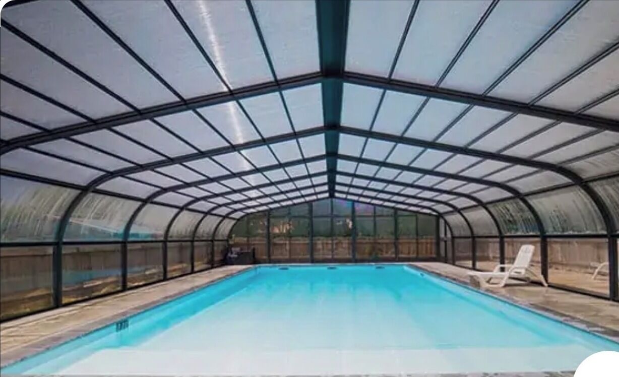 A swimming pool with a glass ceiling, surrounded by lounge chairs.