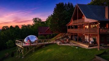 Een houten chalet met twee verdiepingen, een terras, zitplaatsen buiten en een grote bolvormige constructie.