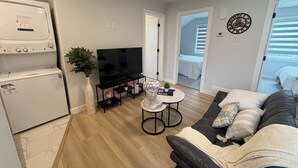 Uma sala de estar moderna com uma TV de tela plana, uma mesa de centro, um sofá e uma área de jantar com uma pequena mesa e cadeiras.