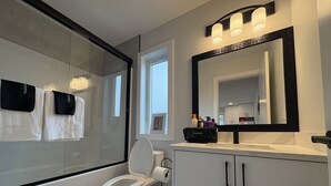 Um banheiro moderno com box de vidro, vaso sanitário, toucador com espelho e janela que permite entrada de luz natural.