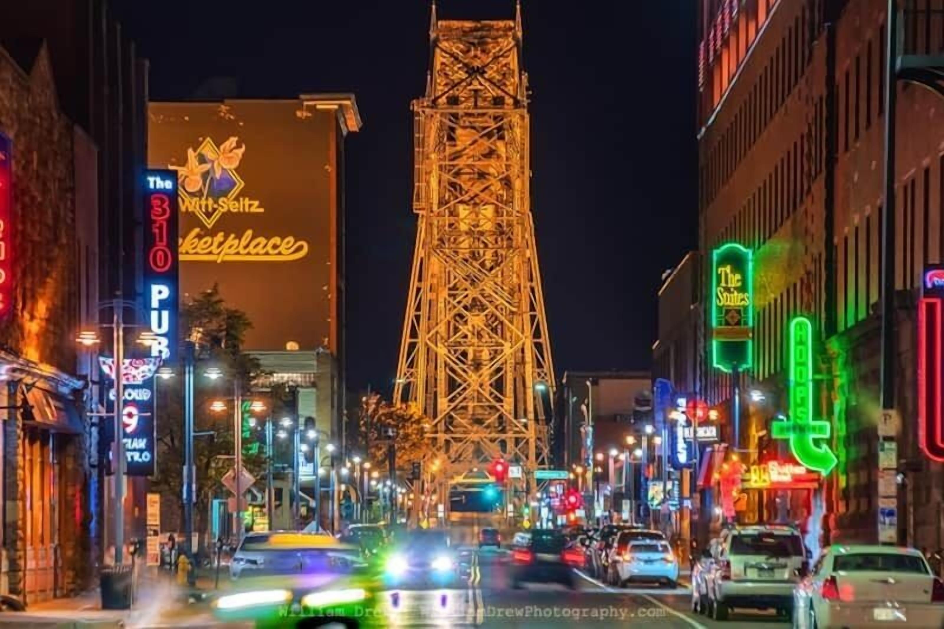 A busy urban street at night with illuminated buildings and a prominent tower structure.
