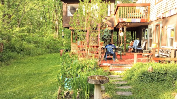 Une terrasse en bois, agréée de mobilier d’extérieur, entourée d’une végétation luxuriante et d’un petit jardin.