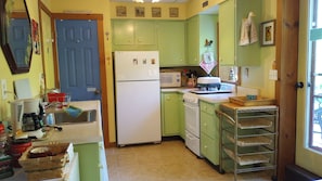 Una cocina con armarios verdes, un refrigerador blanco, un microondas y un lavamanos.