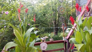 Un jardín con terraza de madera, un comedero de pájaros metálico decorativo y una pequeña vaca de cerámica blanca.
