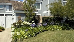 Ein Wohngebäude mit grauer Fassade, einem Ziegeldach und einem gepflegten Garten mit verschiedenen Pflanzen und Blumen.