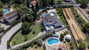 Luchtbeeld van een woonhuis met een zwembad, overdekt terras en tuin.