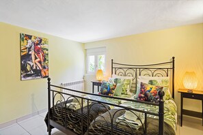 Een slaapkamer met een bed, nachtkastje, lamp, raam en een schilderij aan de muur.