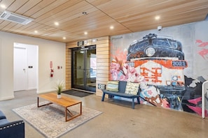Un hall d’entrée avec un plafond en bois, un banc, une table, une fresque murale et un panneau indiquant la sortie.