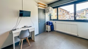 Moderni huone, jossa on työpöytä, tuoli, televisio ja suuri ikkuna, josta on näkymä rakennuksiin.
