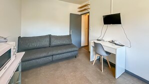 Moderni huone, jossa on harmaa sohva, valkoinen työpöytä, litteänäyttöinen televisio ja riippuvalaisin.
