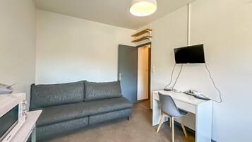 A modern room with a grey sofa, a white desk, a flat-screen TV, and a pendant light.