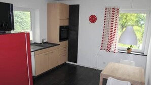 Een compact keuken met een rode koelkast, een spoelbak en een raam met uitzicht op groen.