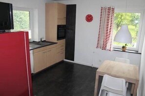 Eine kleine Küche mit einem roten Kühlschrank, einer Spüle und einem Fenster mit Blick auf Grünflächen.