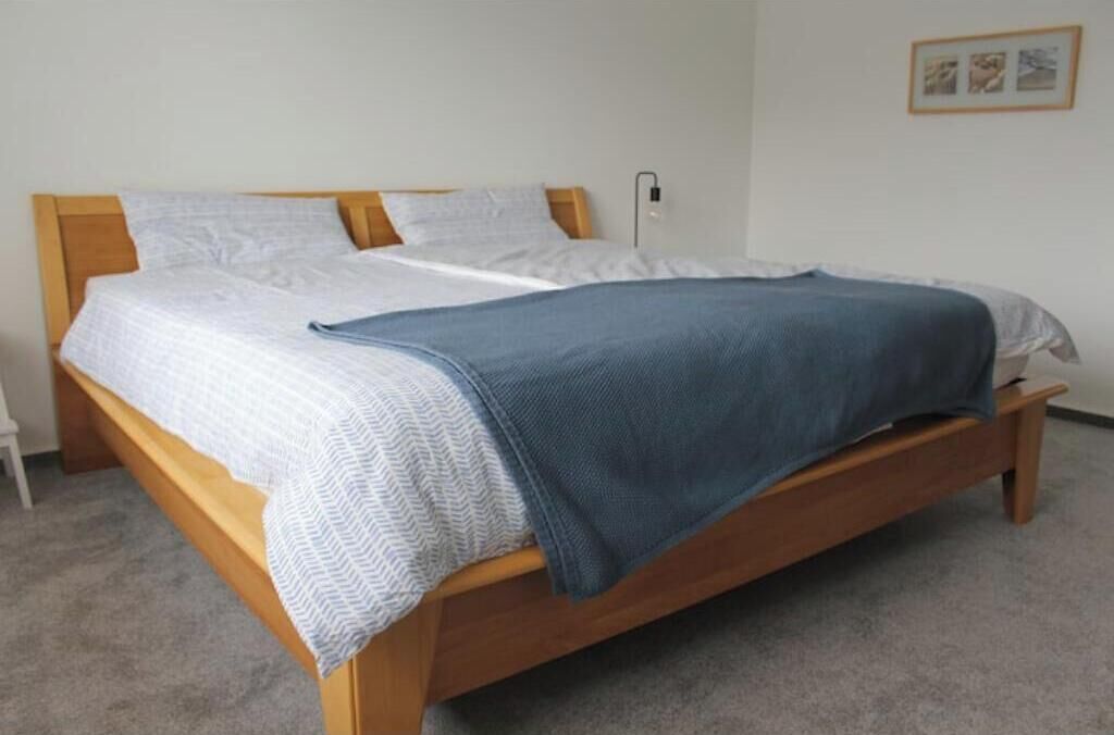 Un lit simple avec un cadre en bois, du linge de lit blanc et une couverture bleue.