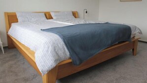 Een enkel bed met een houten frame, wit beddengoed en een blauwe deken.