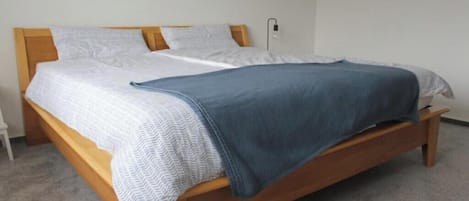 A single bed with a wooden frame, white bedding, and a blue blanket.