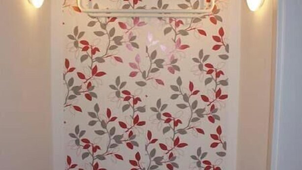Een gang met bloemenbehang, een witte bank en twee wandlampen.