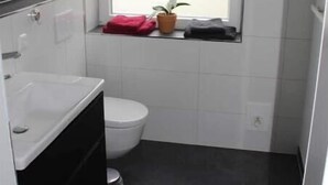 Een kleine badkamer met toilet, wastafel, raam en een potplant.