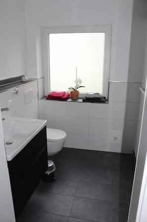 Ein kleines Badezimmer mit Toilette, Waschbecken, Fenster und einer Topfpflanze.