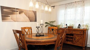 A dining area with a round wooden table, six chairs, a chandelier, a wall-mounted painting, and a wooden cabinet with plants. - Fabulous 5-bedroom house with AC in charming Chickamauga (Chickamauga)