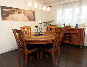 Ein Essbereich mit einem runden Holztisch, sechs Stühlen, einer Kandelaber, einem Wandbild und einer Holzvitrine mit Pflanzen.