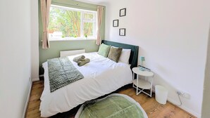 Un lit bien fait, avec des oreillers, une table de chevet avec une lampe, une fenêtre avec des rideaux et un radiateur.