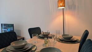 Une table à manger dressée avec des bols, des verres et des couverts, un téléviseur en arrière-plan et une lampe sur pied.