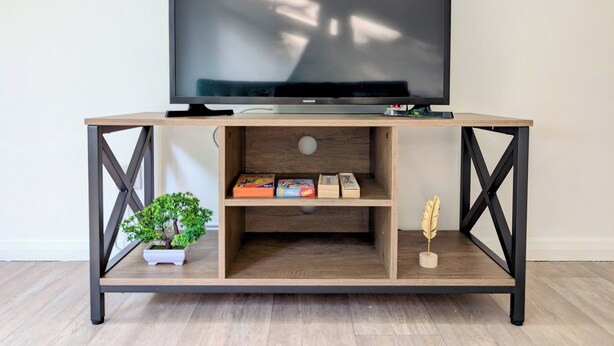 Un téléviseur posé sur un meuble TV en bois, doté d’étagères, une petite plante et un objet décoratif.