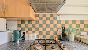 Une cuisine équipée d’une cuisinière à gaz, d’une bouilloire et d’un crédence à carreaux.