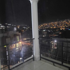 Ein Balkon mit Blick auf eine nächtliche Stadtlandschaft.