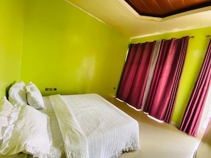 Una habitación con cama, paredes verdes y cortinas rojas.