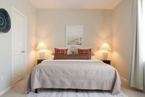 Un dormitorio con una cama, dos lámparas de noche, un cuadro enmarcado encima de la cama y una puerta a la izquierda.