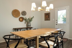 Un comedor con una mesa de madera, sillas negras, una araña y adornos en la pared.