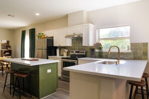 Cocina moderna con una isla central, taburetes de bar, un refrigerador de acero inoxidable y una ventana con vistas a zonas verdes.